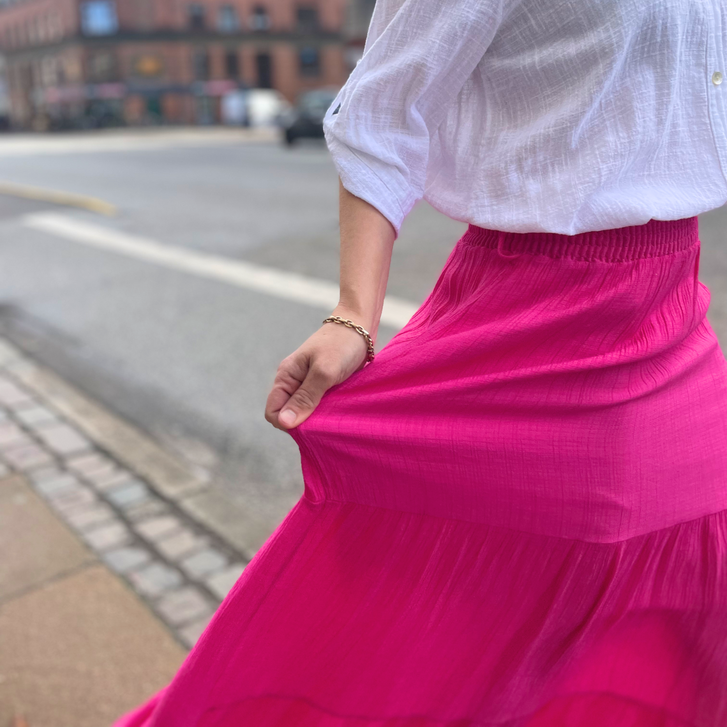 Hvid bluse møder iøjnefaldende pink nederdel – en livlig kontrast, der er både dristig og afslappet. Perfekt til sommerdage og lysere aftener.